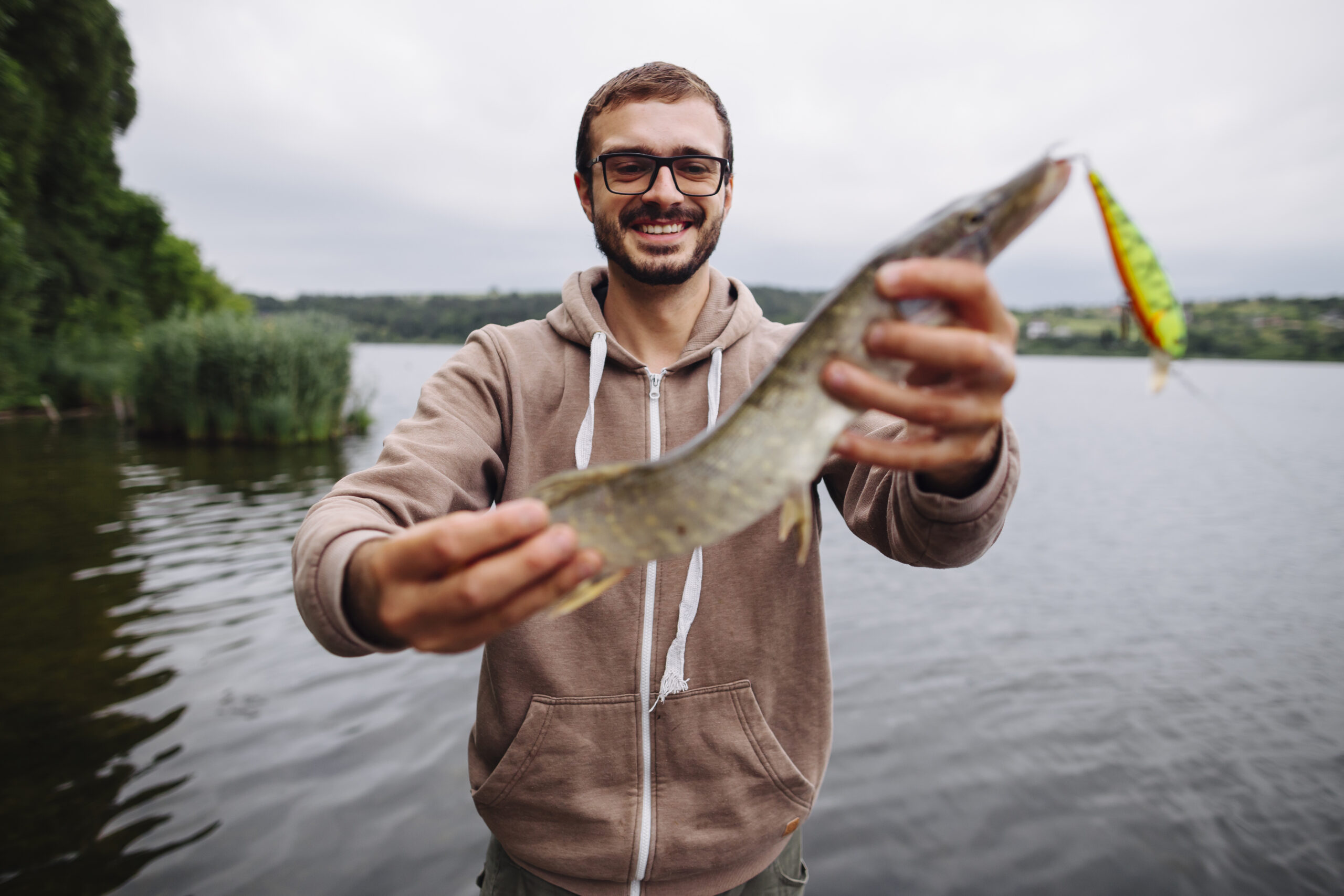 smiling young man holding fresh water fish with lure scaled